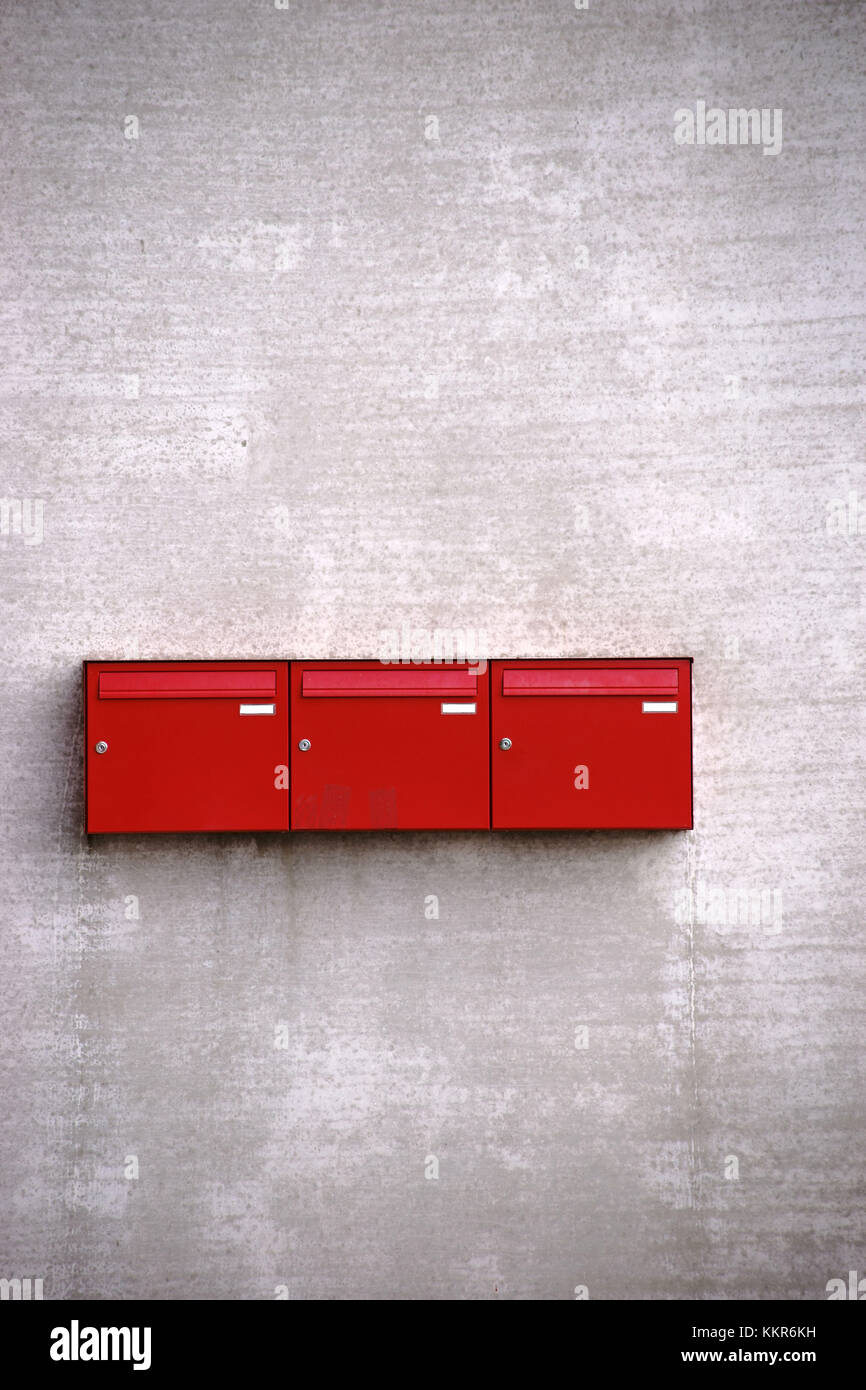 Tre caselle di posta rosse in fila sulla facciata in cemento ruvida di un edificio. Foto Stock