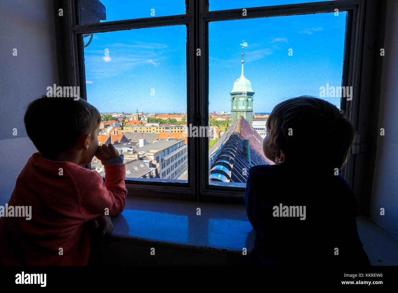 Due bambini guardano la Chiesa di Trinitatis da una finestra all'interno della Torre rotonda (Rundetaarn), Copenhagen, Danimarca Foto Stock