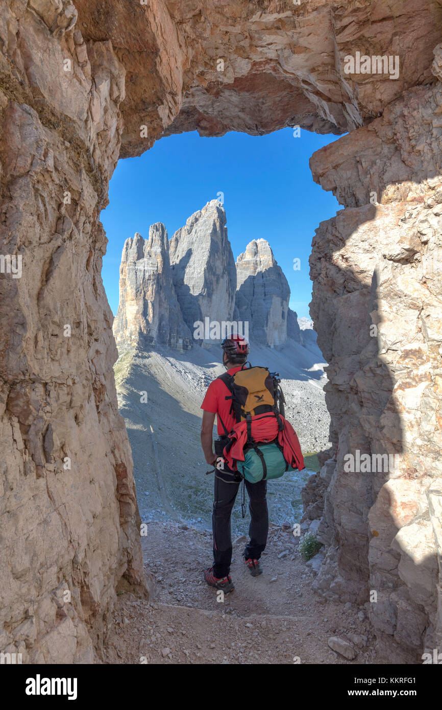 Escursionista cercando le tre cime di lavaredo / Drei Zinnen attraverso una finestra nella roccia ai piedi del monte paterno / paternkofel, sesto dolomiti alto adige, bolzano, Italia Foto Stock
