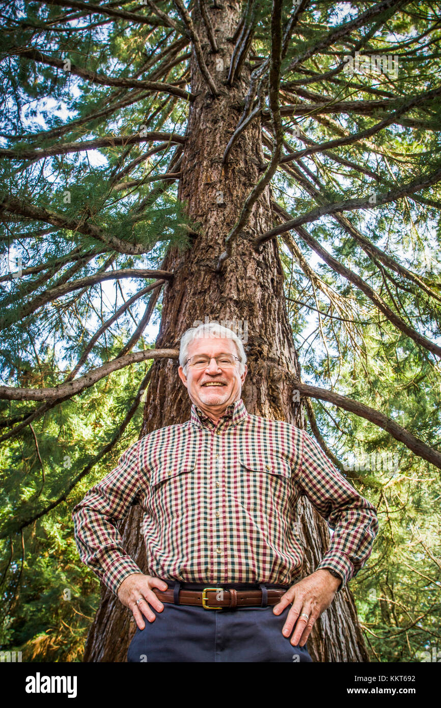 Un ritratto di un uomo maturo in piedi sotto un grande albero sorridente. Foto Stock