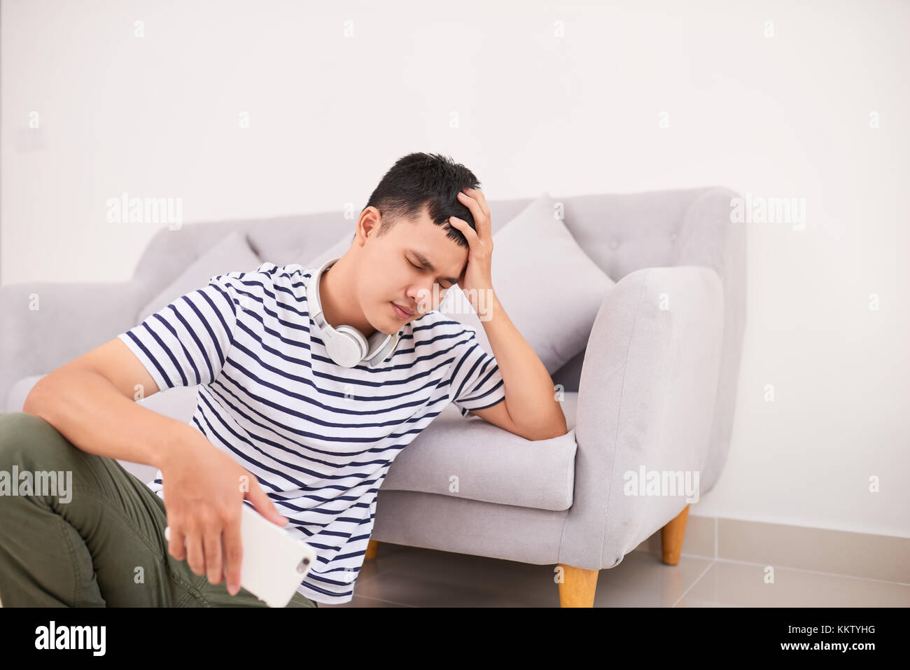Disperato giovane uomo seduto sul pavimento dello smartphone di contenimento Foto Stock
