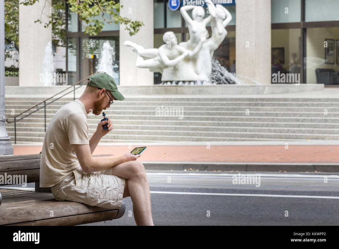 Portland, Oregon, USA - 9 settembre 2017: Un uomo siede a fumare una sigaretta elettronica e guarda il suo cellulare per strada a Seattle. Foto Stock