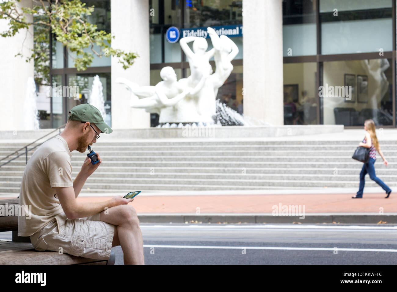 Portland, Oregon, USA - 9 settembre 2017: Un uomo siede a fumare una sigaretta elettronica e guarda il suo cellulare per strada a Seattle. Foto Stock