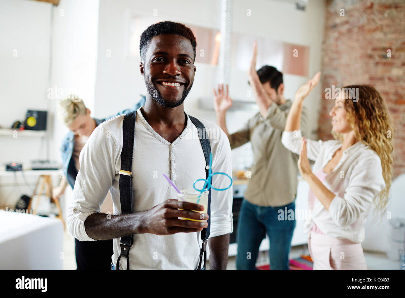 Felice AFRICAN-AMERICAN guy con drink osservando camer aon sfondo di ballare gli amici Foto Stock