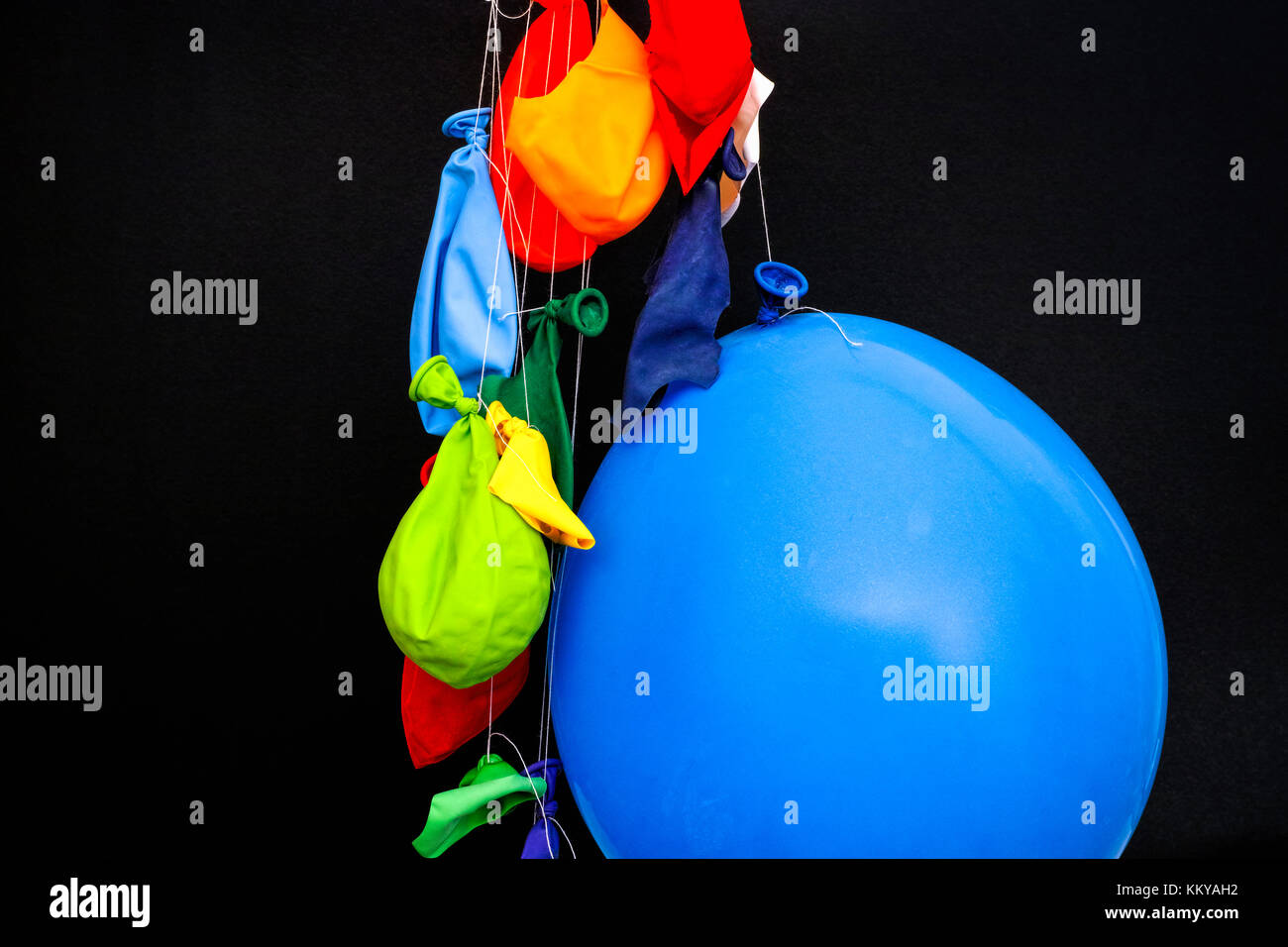 La fine di una festa. Alcuni burst, palloncini sgonfi e un palloncino gonfiato appeso sul thread. sfondo nero. Foto Stock
