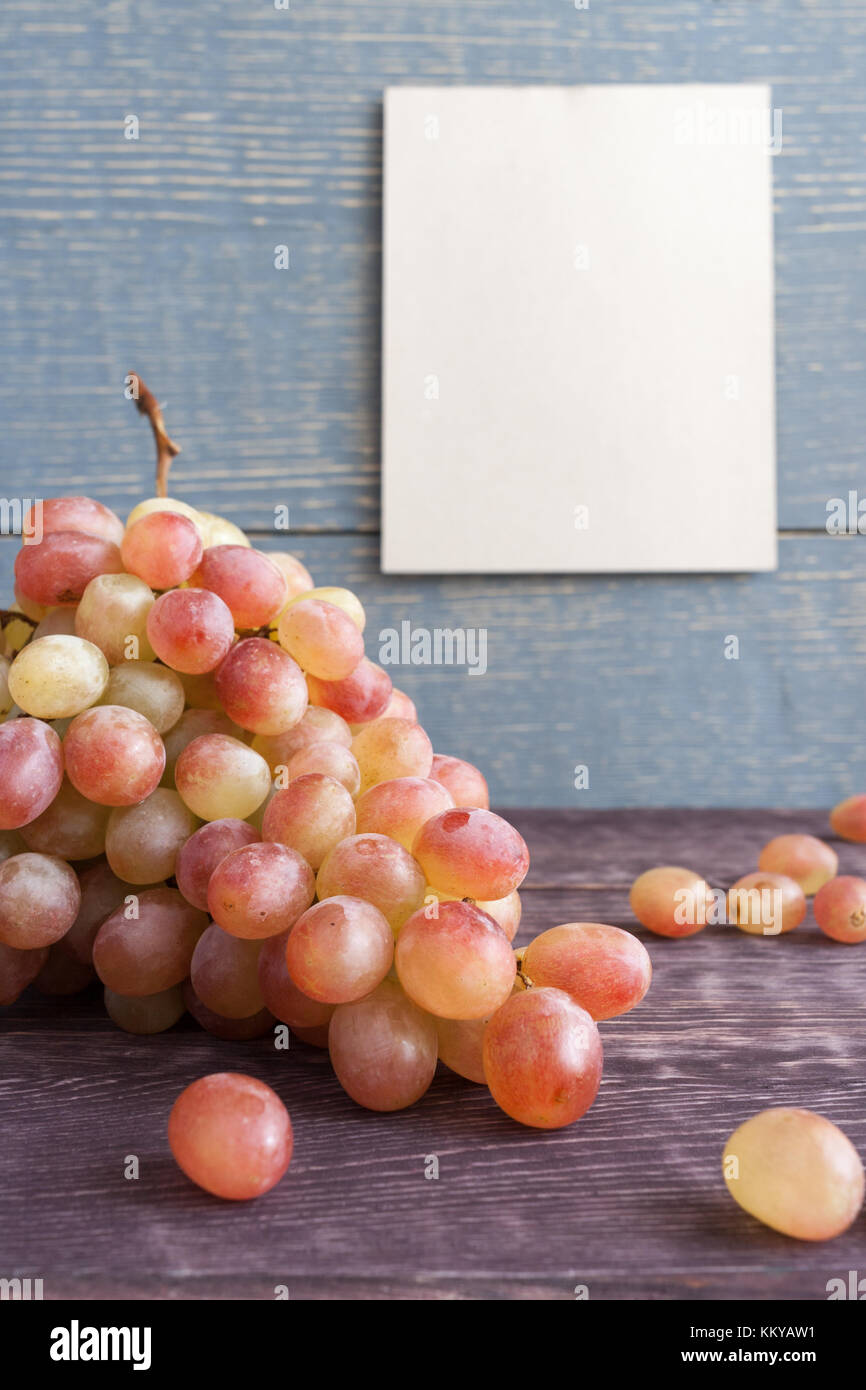 Infiorescenza staminifera di ripe rosso-giallo uve è disteso sul legno scuro tavolo. Sfondo grigio di tavole di legno con vuoto foglio pulito. Foto Stock