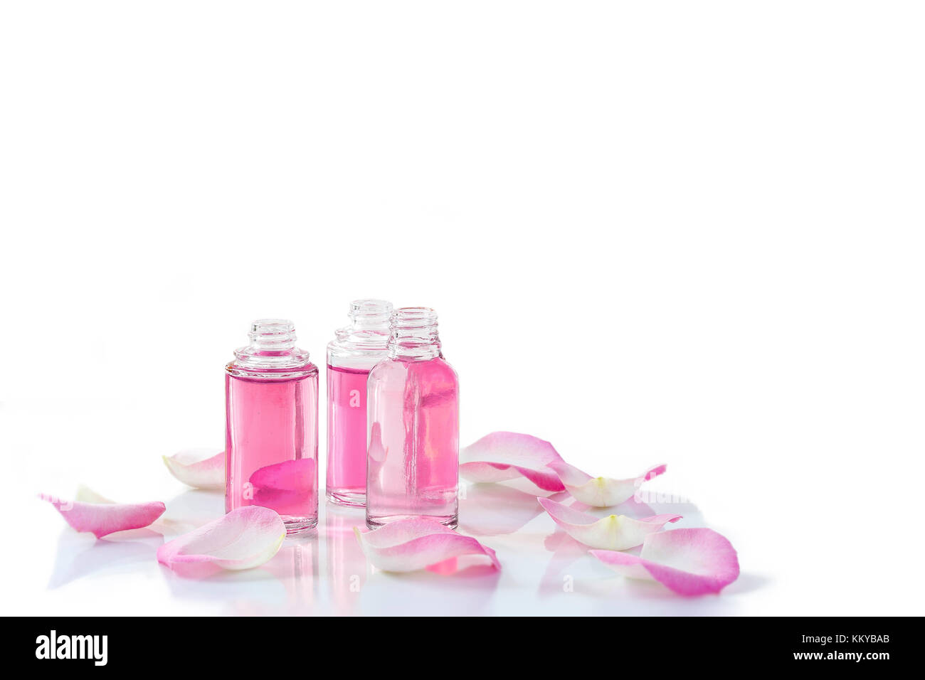 Una bottiglia di rosa olio essenziale con petali di rosa su sfondo bianco Foto Stock