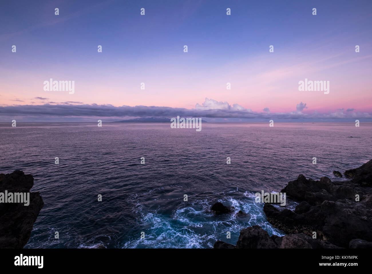 Mare turbinano intorno rocce sulla costa occidentale di Tenerife e La Gomera all'orizzonte, sotto un cielo viola all'alba, Isole Canarie, Spagna Foto Stock