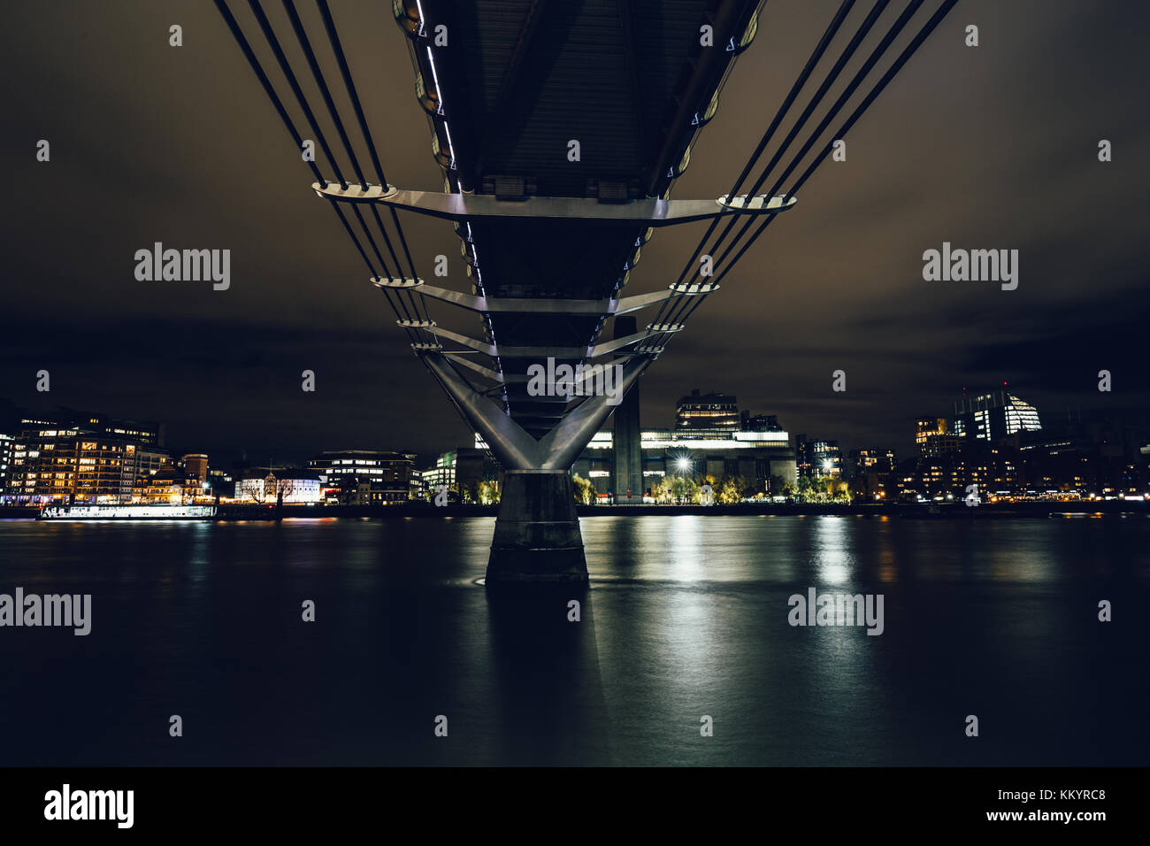 Una lunga esposizione shot prese sotto il Millennium Bridge sul fiume Tamigi a Londra presso moody notte Foto Stock