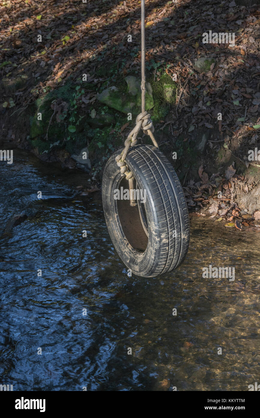 Vecchia ruota di pneumatico di automobile / swing del pneumatico a riposo sopra un flusso di paese - ricorda uno di divertimento di infanzia e anche metafora per le oscillazioni del pendolo. Foto Stock