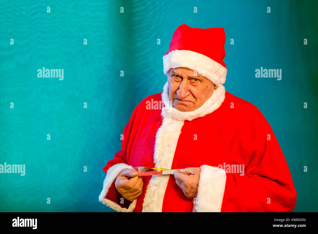 Triste vecchio uomo che indossa Santa Claus costume la misurazione della circonferenza del suo ventre con un nastro di misurazione Foto Stock