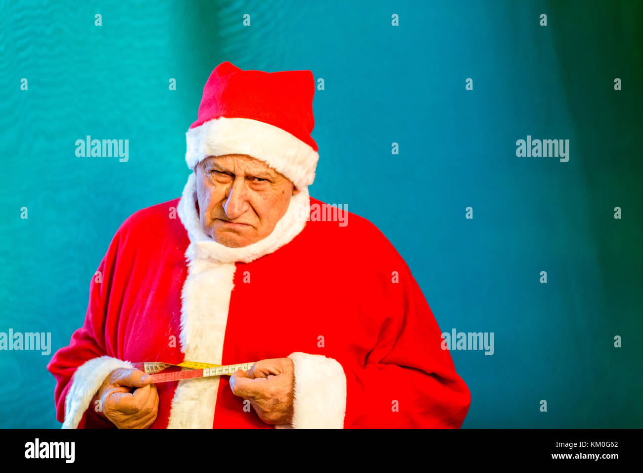 Il vecchio uomo che indossa Santa Claus costume di piangere e la misurazione della circonferenza del suo ventre con un nastro di misurazione Foto Stock