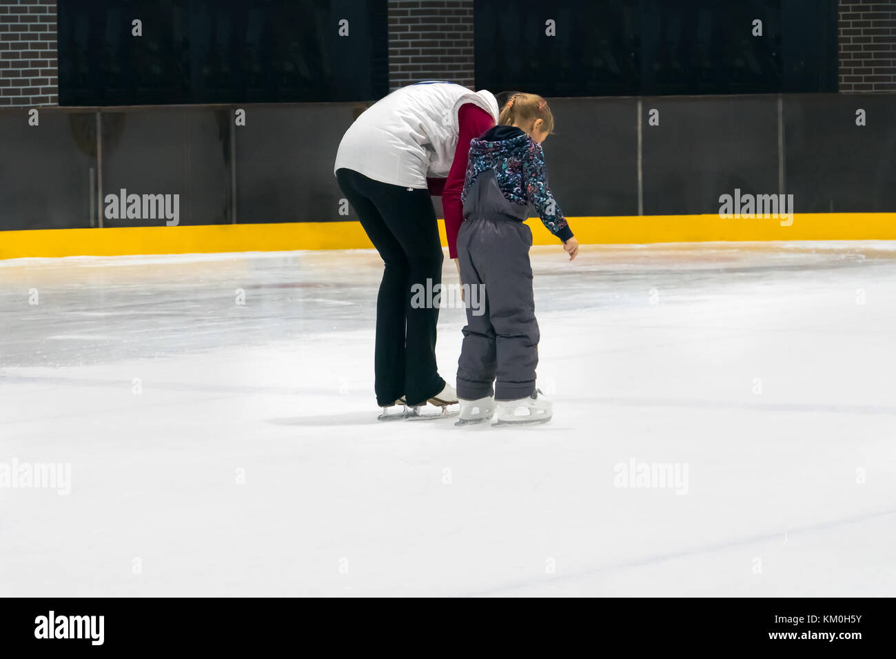 La famiglia felice indoor pattinaggio su ghiaccio a rink. attività invernali. ragazza giovane istruttore insegna una bambina a pattino. madre e figlia per mano Foto Stock