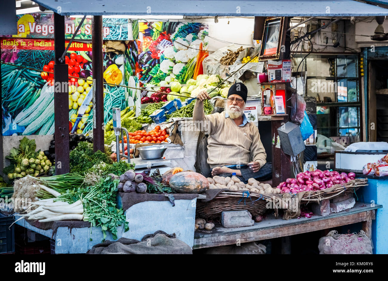 Maschio locale stallholder Sikh seduto a gambe incrociate in un negozio di vegetali, Amritsar e una città nel nord-occidentale dell'India nella regione di Majha del Punjab Foto Stock