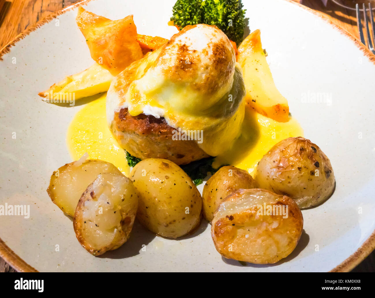 Pranzo in un ristorante francese in Inghilterra una fishcake su spinaci con un uovo in camicia e salsa olandese servita con verdure e arrosto di patate primaticce Foto Stock