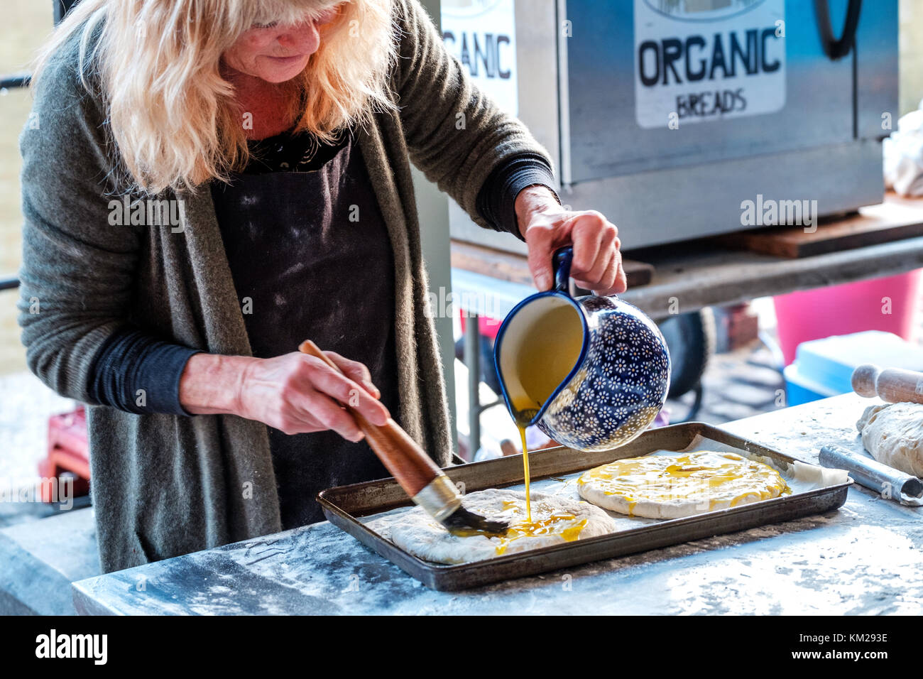 Una femmina di baker si prepara la focaccia italiana pane piatto in una stalla all'aperto ella è versando olio sulla parte superiore dell'impasto prima di essa è collocata in un forno per cucinare Foto Stock