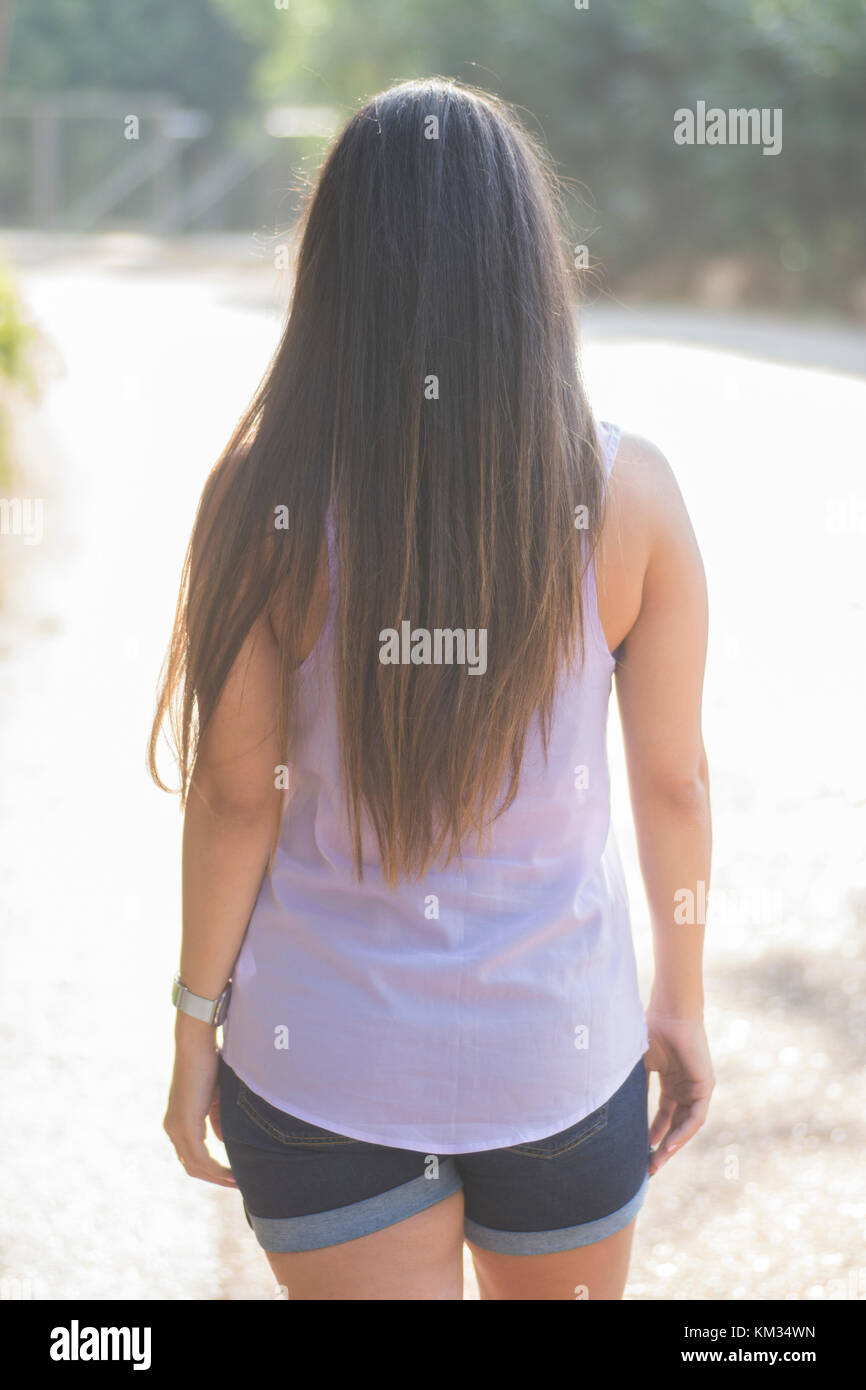 Vista posteriore di una giovane donna con lunghi capelli scuri in piedi all'aperto Foto Stock