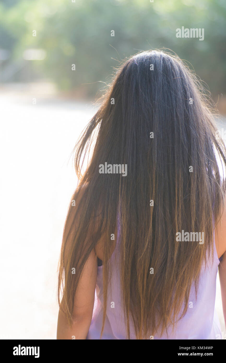 Vista posteriore di una giovane donna con lunghi capelli scuri in piedi all'aperto Foto Stock