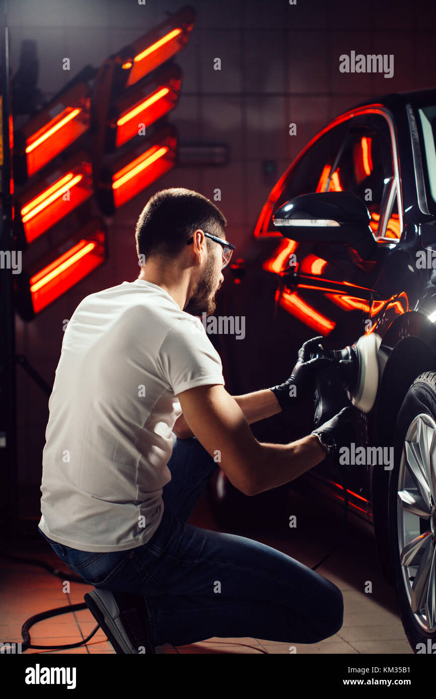 Dettagli auto - uomo con lucidatrice orbitale nel negozio di riparazioni auto. Il fuoco selettivo. Foto Stock