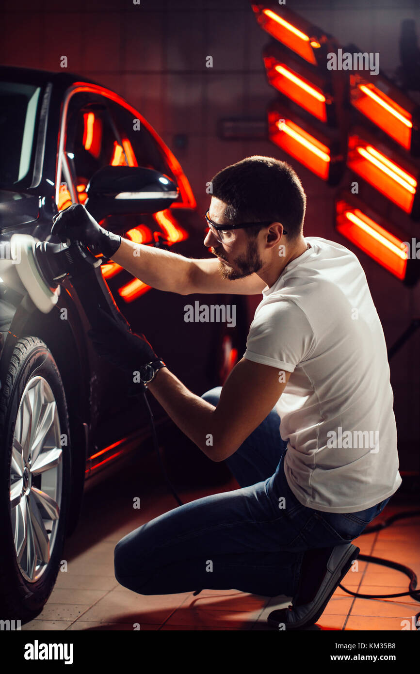 Dettagli auto - uomo con lucidatrice orbitale nel negozio di riparazioni auto. Il fuoco selettivo. Foto Stock