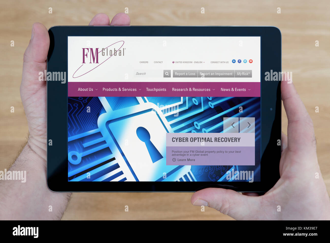 Un uomo guarda presso FM Global sito di assicurazione sul suo iPad dispositivo tablet, sparato contro un tavolo di legno top sfondo (solo uso editoriale) Foto Stock