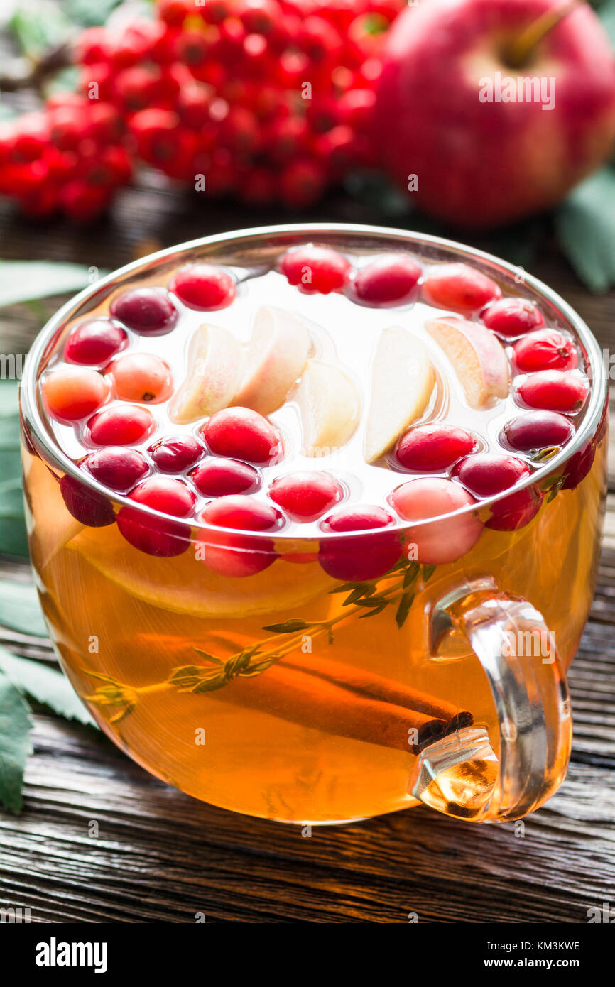 Inverno berry tè con mirtilli rossi, Apple, cannella, limone, il miele e il timo in un bicchiere di vetro su un tavolo di legno. In orizzontale e di primo piano Foto Stock