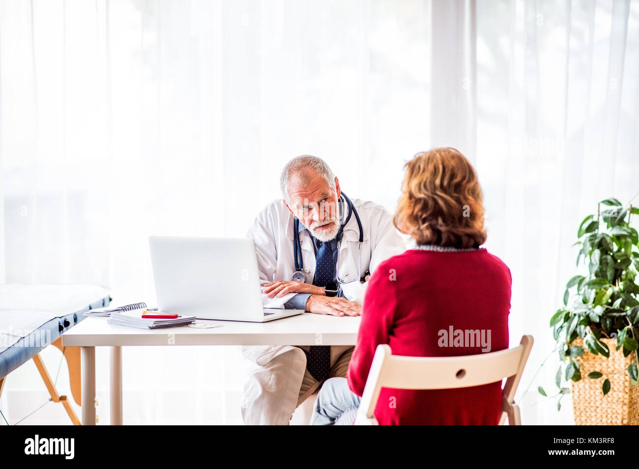 Medico con laptop a parlare con una donna senior in ufficio. Foto Stock