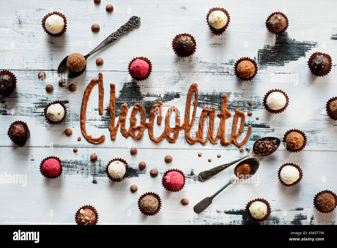 Parola cioccolato fatto da vetri con cioccolatini, caramelle e cucchiaini da tè su un bianco sullo sfondo di legno. Alimentare il concetto di tipografia. Foto Stock