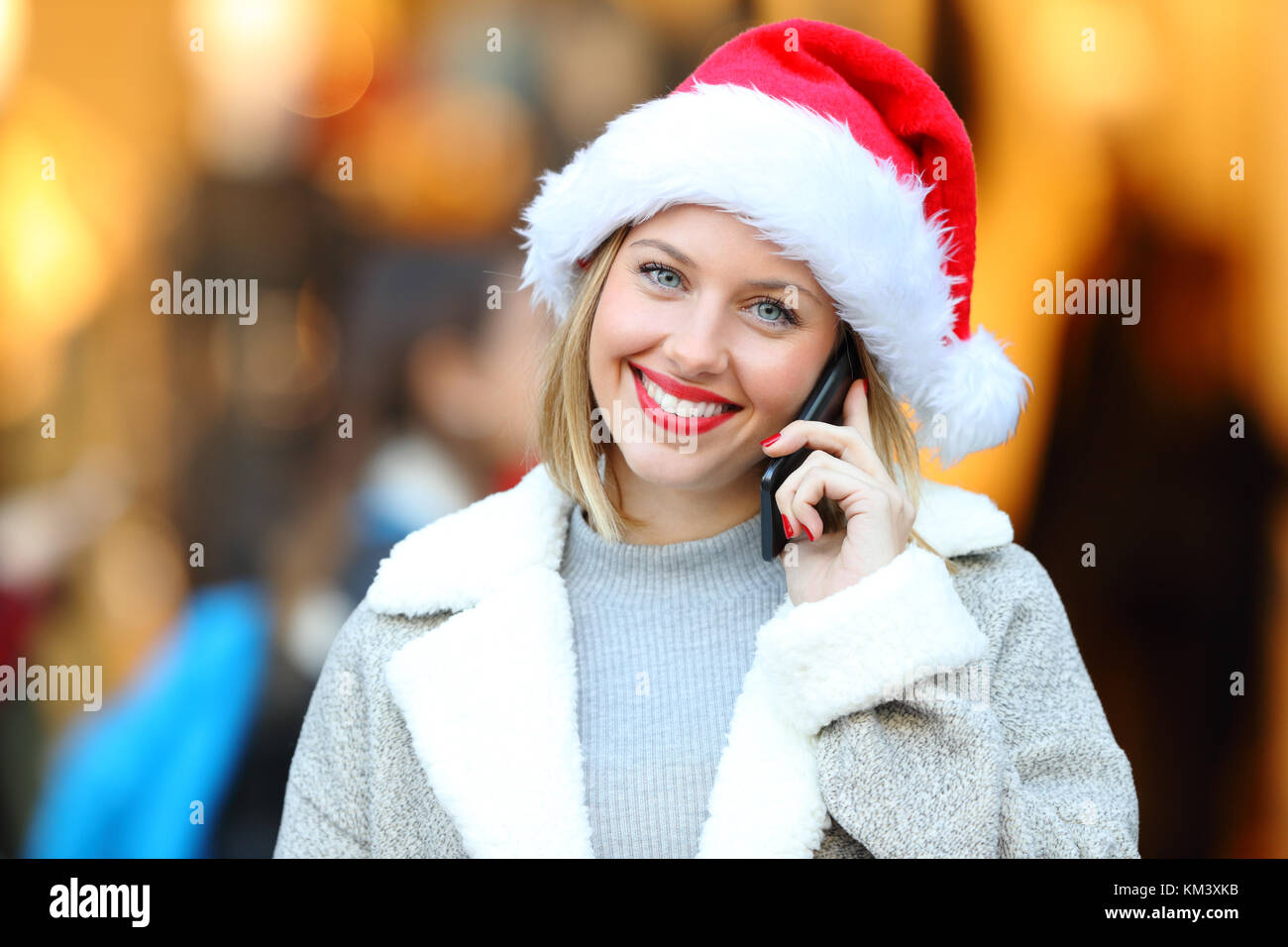 Vista frontale ritratto di una ragazza chiamata sul cellulare e guardando a voi in vacanze di Natale sulla strada con una vetrina in background Foto Stock