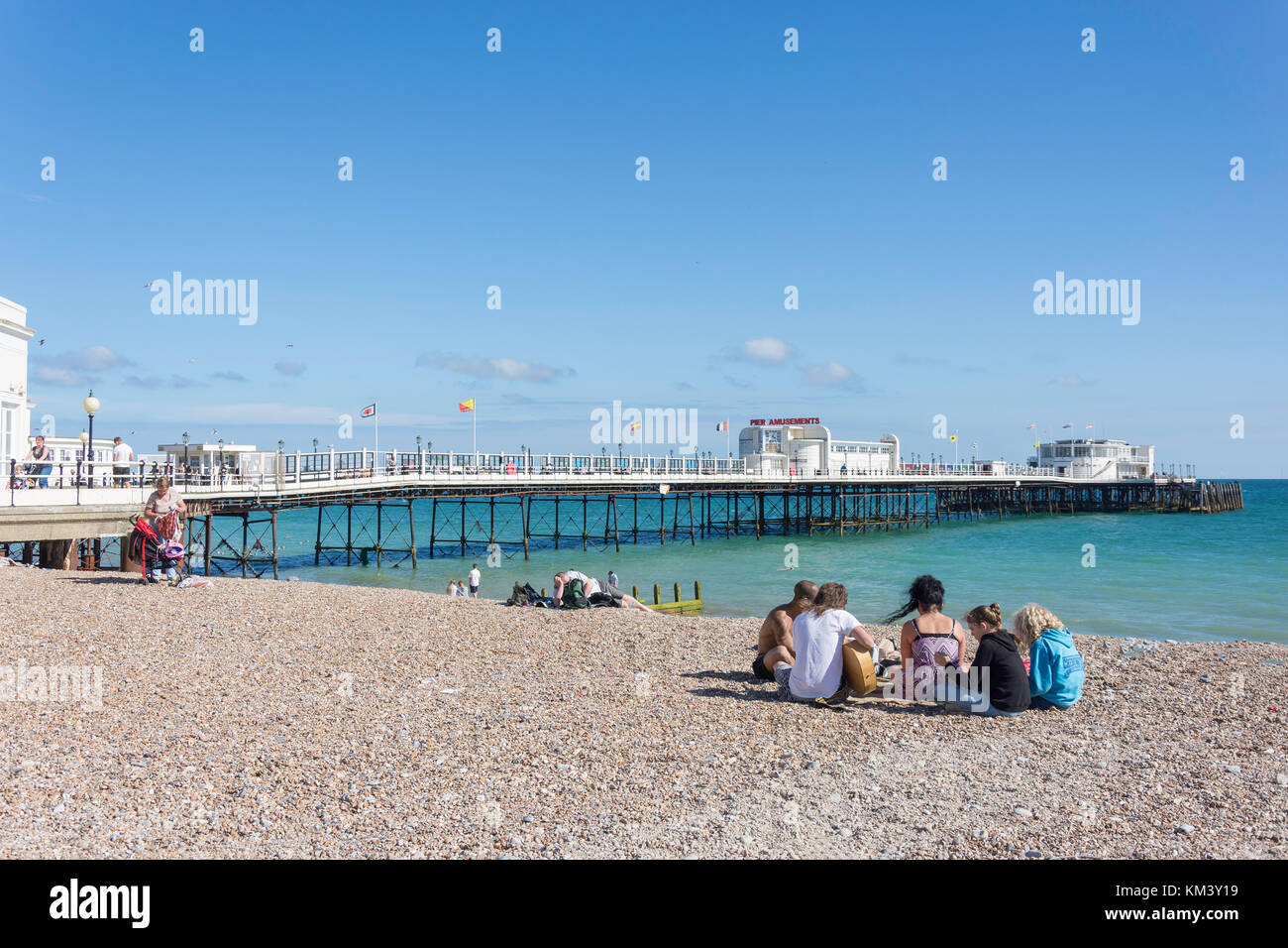 Gruppo di giovani sulla spiaggia con Worthing Pier dietro, Worthing, West Sussex, in Inghilterra, Regno Unito Foto Stock