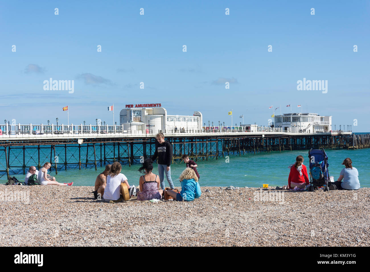 Gruppo di giovani sulla spiaggia con Worthing Pier dietro, Worthing, West Sussex, in Inghilterra, Regno Unito Foto Stock