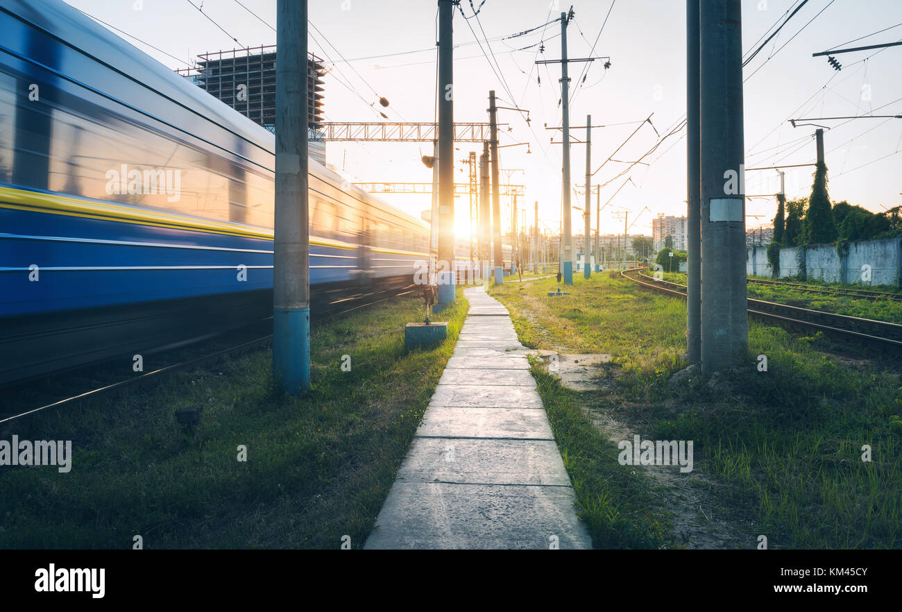 Ad alta velocità per i passeggeri il treno in movimento su ferrovia via al tramonto. Stazione ferroviaria con sfocato moderno treno dei pendolari in serata in Europa. Industr Foto Stock