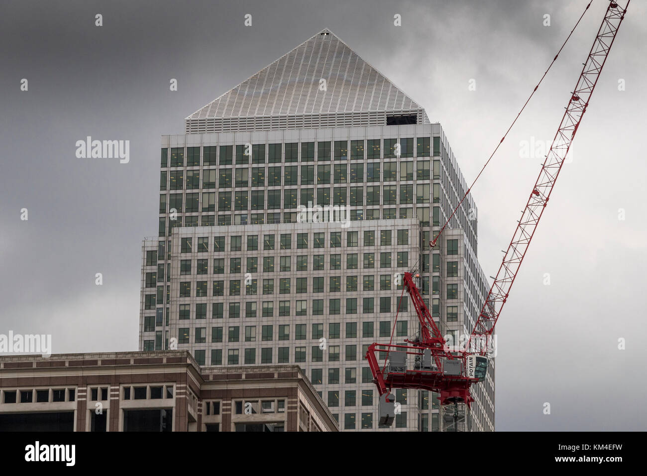 Una gru in cantiere al lavoro si affaccia sulla gigantesca torre di One Canada Square, Canary Wharf, Docklands, Londra, Regno Unito Foto Stock