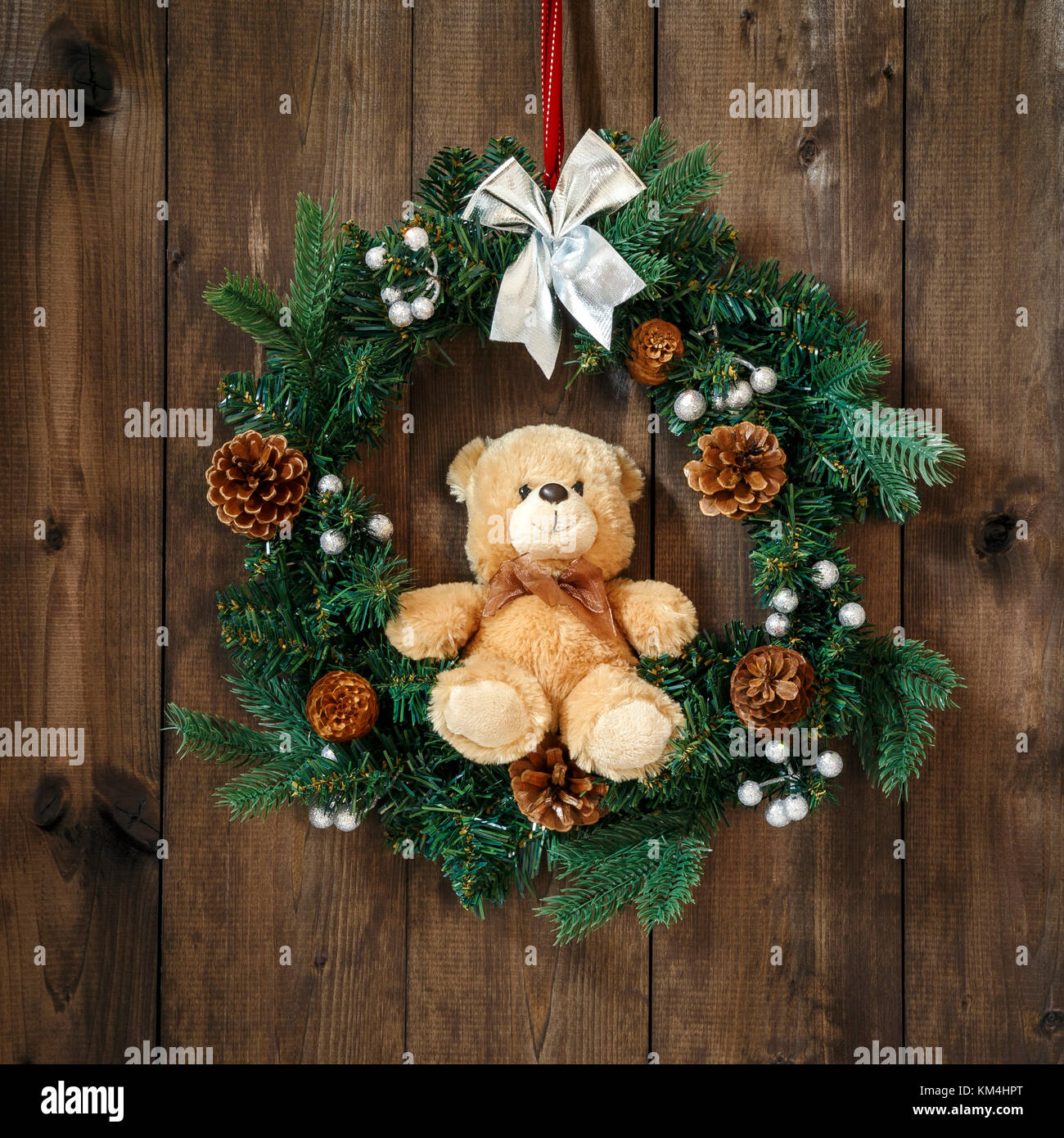 Appendere decorata corona di Avvento sul nastro rosso con argento di prua e con seduta orsacchiotto di peluche su un sfondo di legno. Foto Stock