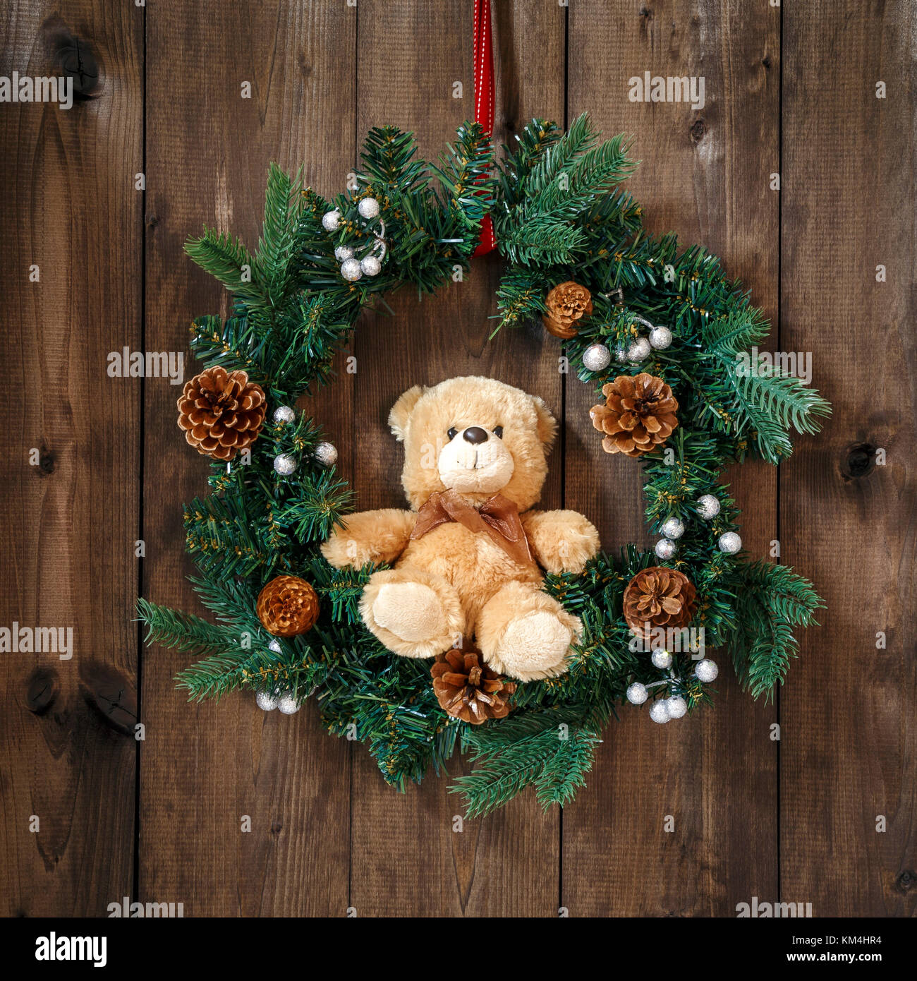 Appendere decorata corona di Avvento sul nastro rosso con seduta orsacchiotto di peluche su un sfondo di legno. Foto Stock