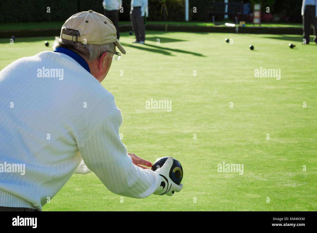 Un prato giocatore di bocce indossando un guanto, azienda e preparazione per offrire una ciotola giù verde l'erba liscia superficie di gioco. Foto Stock
