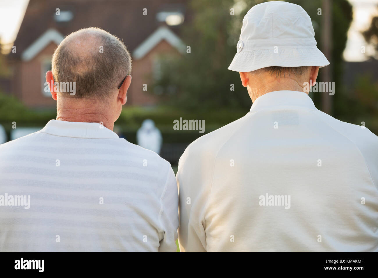 Due compagni, due uomini stavano in piedi a fianco a fianco in camice bianco all'esterno. prato giocatori di bocce, uno in un cappello per il sole. Foto Stock