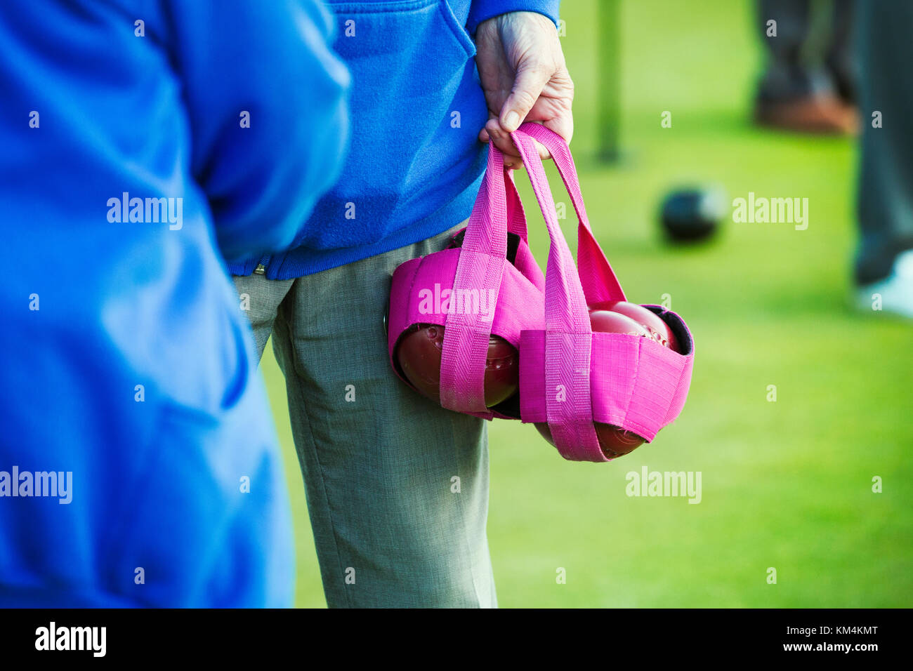 Due persone in blu camicie, uno che porta quattro legno bocce su prato in un sacchetto di colore rosa. Foto Stock