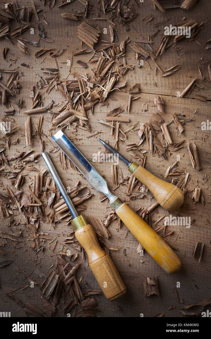 Tre attrezzi di mano, scalpelli di varie forme e un punteruolo in trucioli sulla superficie di un pezzo di legno piallato. Foto Stock