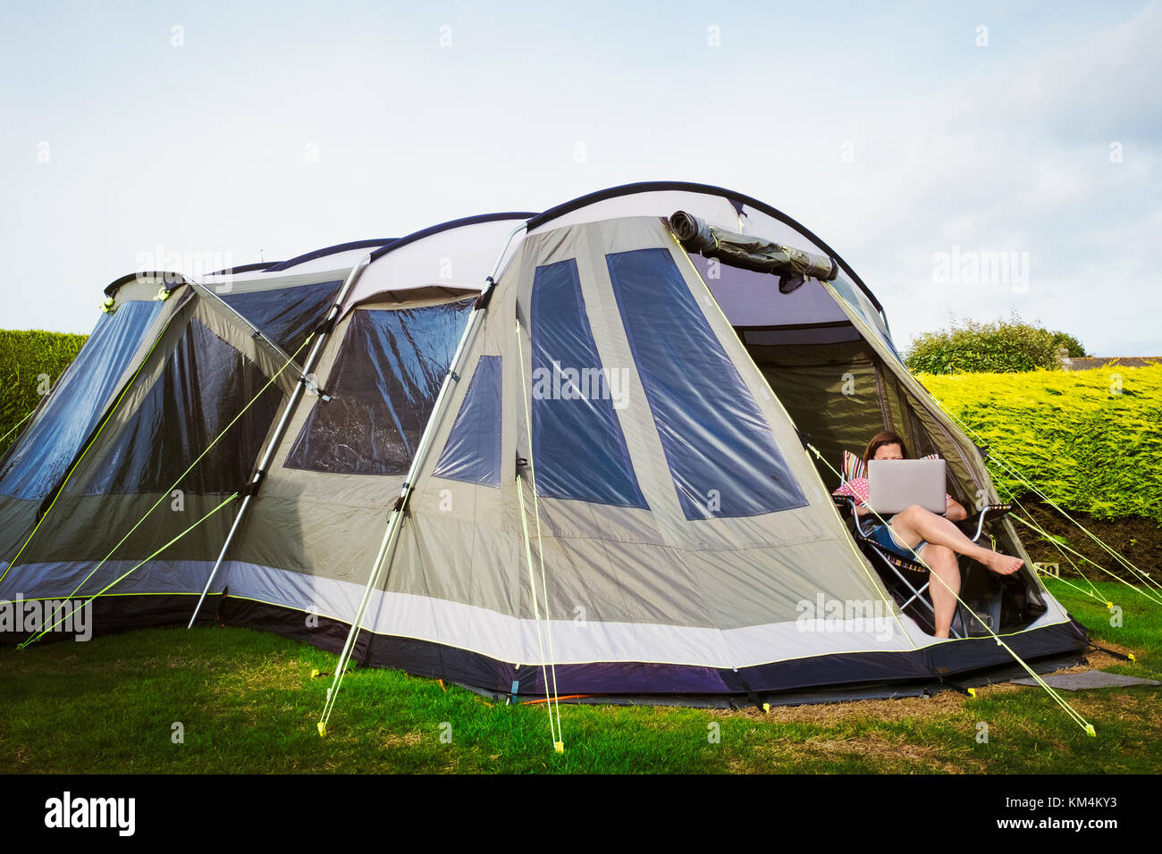 Donna seduta su una sedia davanti alla porta di una grande tenda in un campeggio, usando un computer portatile. Foto Stock