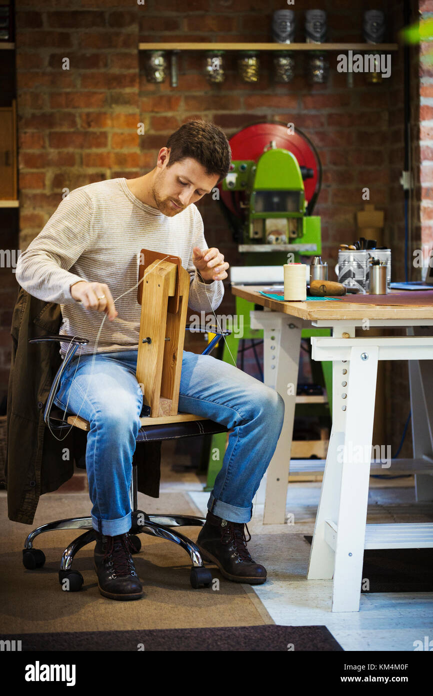 Un artigiano leatherworker seduto nella sua bottega, cucire insieme un piccolo oggetto in pelle. Foto Stock