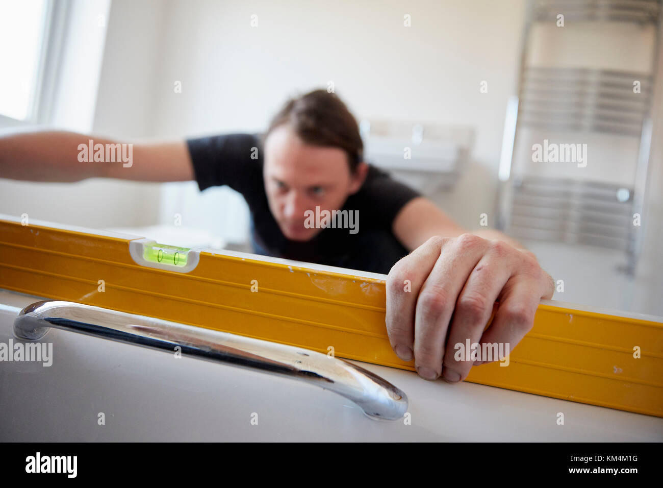 Un costruttore utilizzando una livella a bolla per controllare il suo lavoro, refurbushing un bagno. Foto Stock