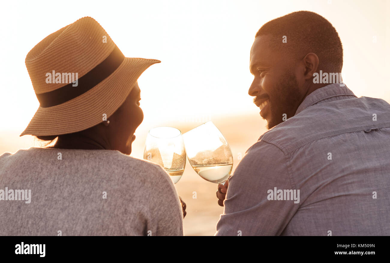 Felice coppia africana di bere vino e guardare il tramonto sulla spiaggia Foto Stock