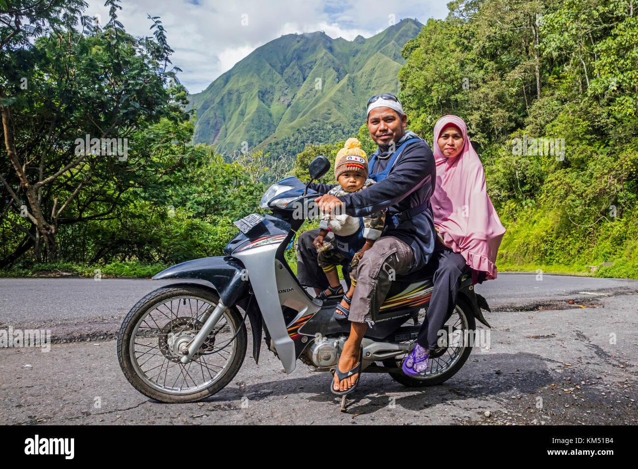 Famiglia indonesiana con moto per bambini attraverso la foresta pluviale tropicale sulle pendici del Monte Rinjani, vulcano sull'isola di Lombok, Indonesia Foto Stock