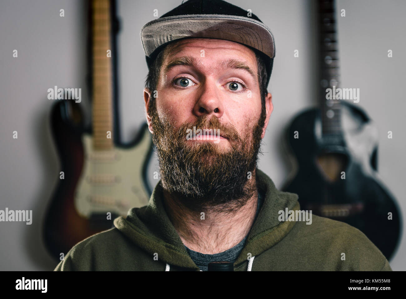 Giovane uomo bello barbuto hipster con la barba e baffi ritratto. Moderna, casual cercando, occhi blu musicista ragazzo con un cappello e una elettrica e acous Foto Stock