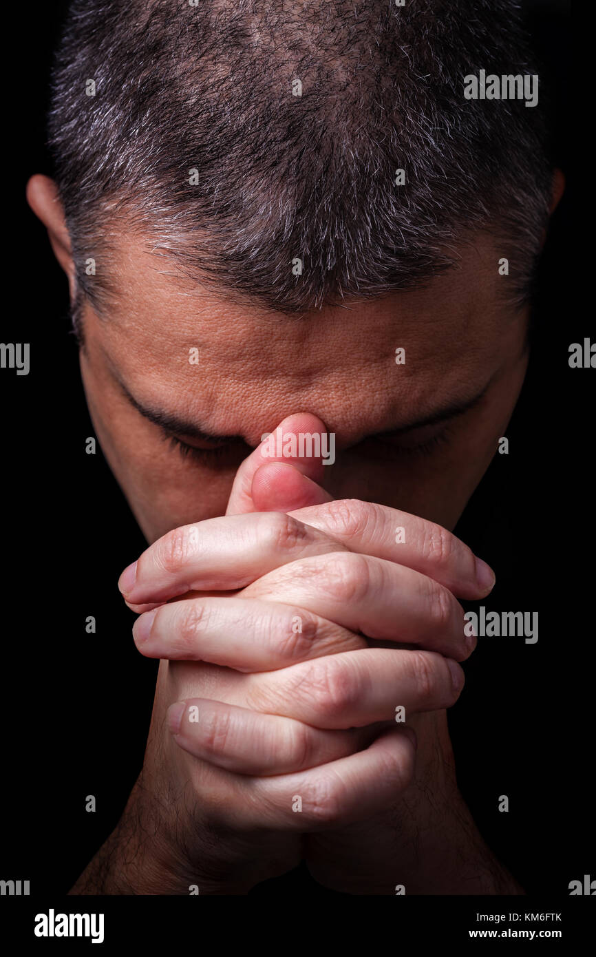 Close up di fedeli uomo maturo pregando mani giunte adorare DIO a testa in giù e gli occhi chiusi in religioso sfondo nero la religione cristiana ritratto Foto Stock