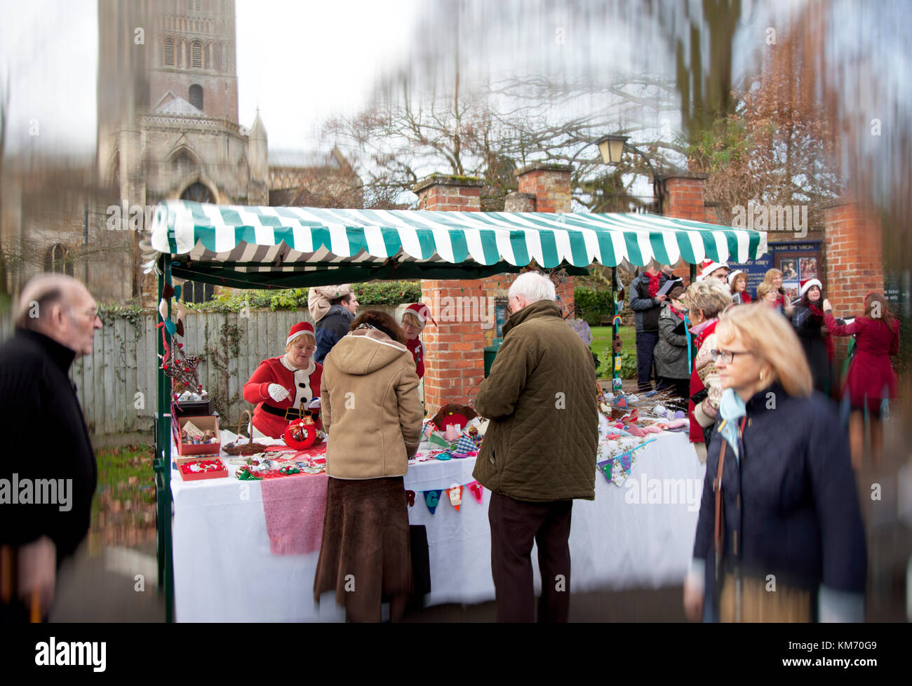 I titolari di stallo vestito come santa presso gli agricoltori e imbarcazione di mercato al di fuori di Tewkesbury Abbey con Natale carol cantanti Foto Stock