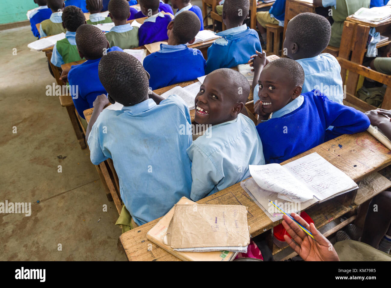 I bambini della scuola secondaria in uniforme si sedettero a scrivanie di legno sorridenti alla telecamera durante la lezione, Nairobi, Kenya Foto Stock