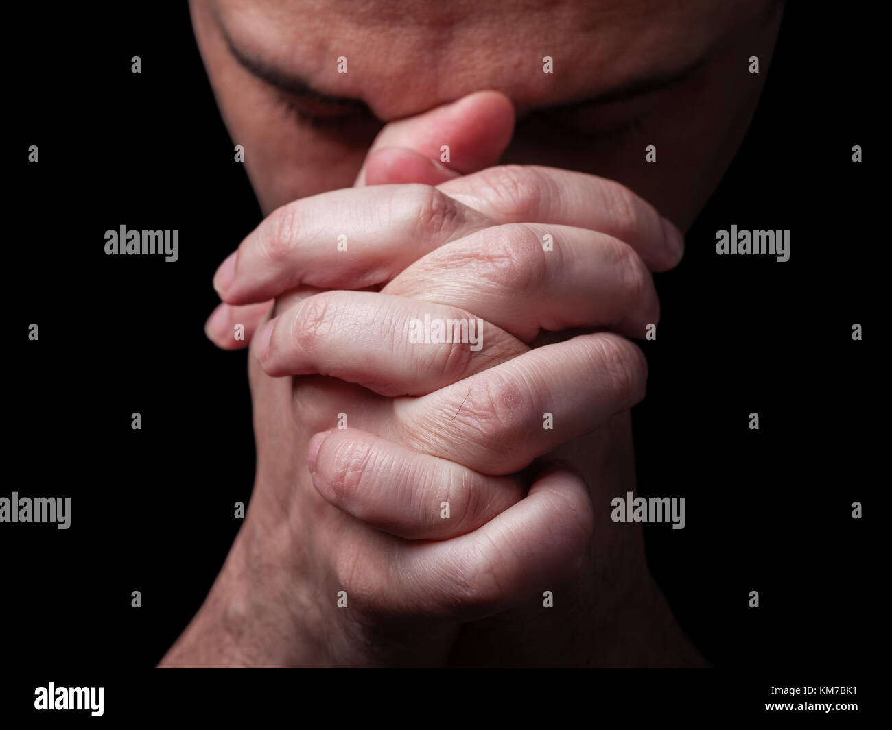 Close up di fedeli uomo maturo pregando mani giunte adorare DIO a testa in giù e gli occhi chiusi in religioso sfondo nero la religione cristiana ritratto Foto Stock