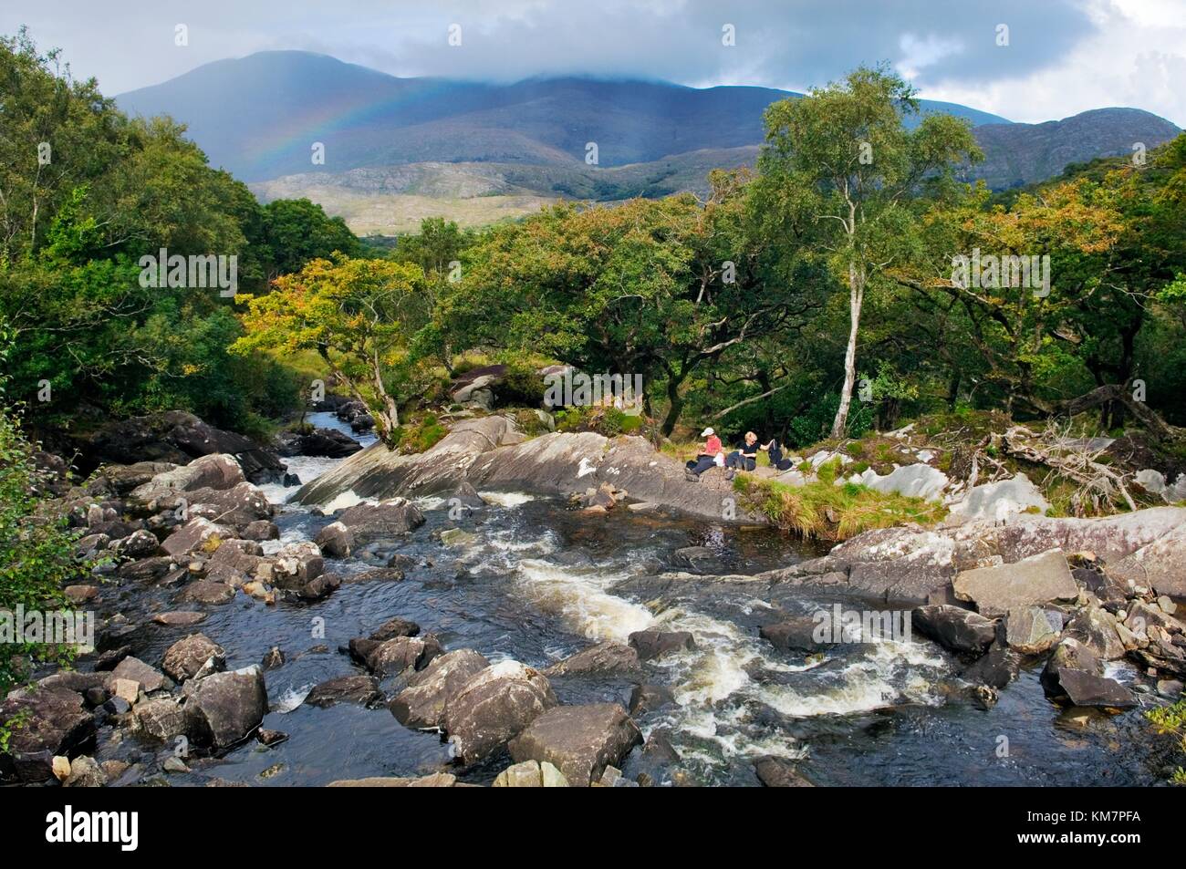 Giovane uomo e donna picnic accanto a Galway's River a Galway il ponte sopra il lago Superiore, Parco Nazionale di Killarney, Co.Kerry, Irlanda Foto Stock